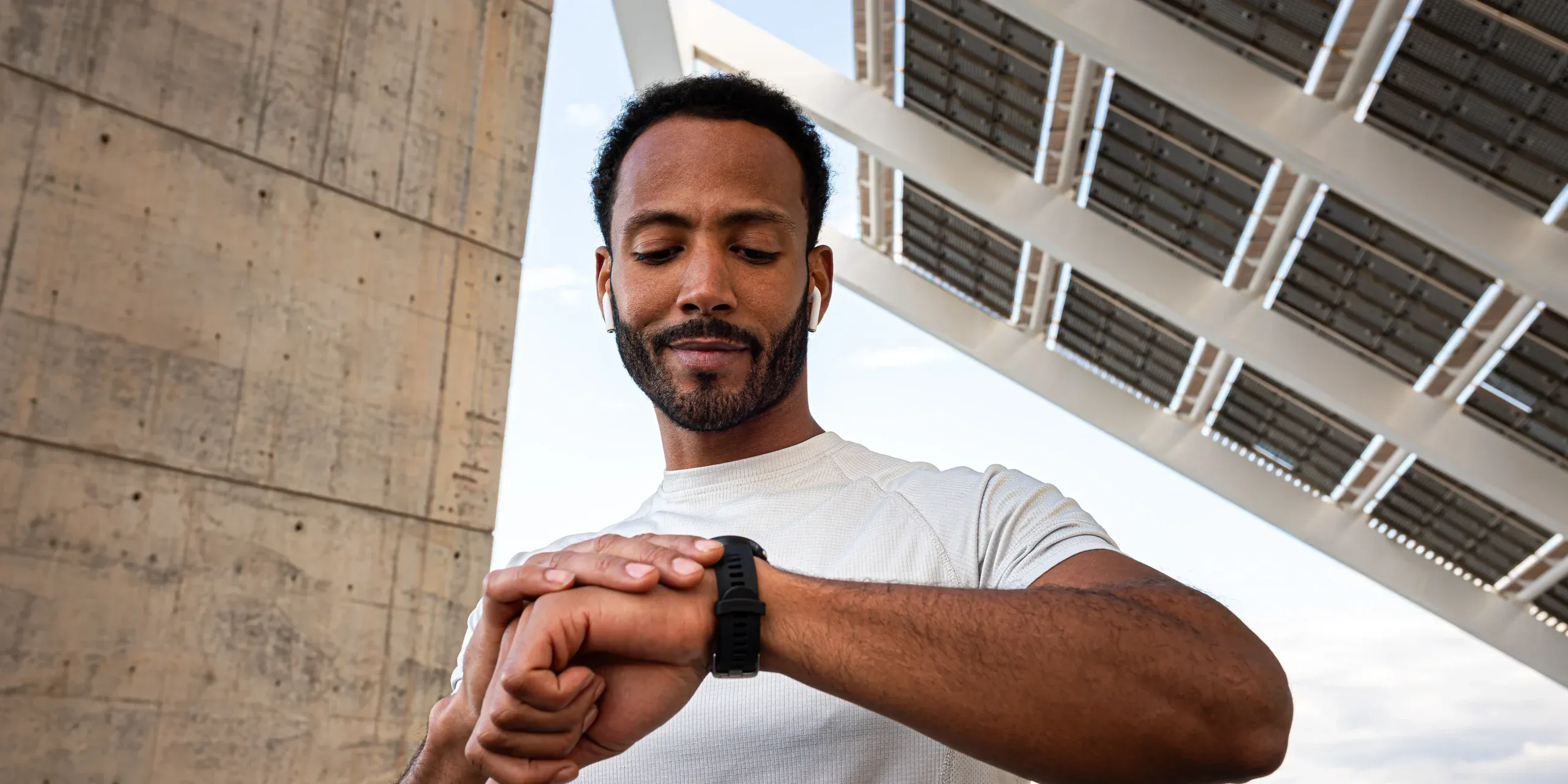 A man in athletic wear checking his smartwatch while wearing wireless earbuds during an outdoor workout.