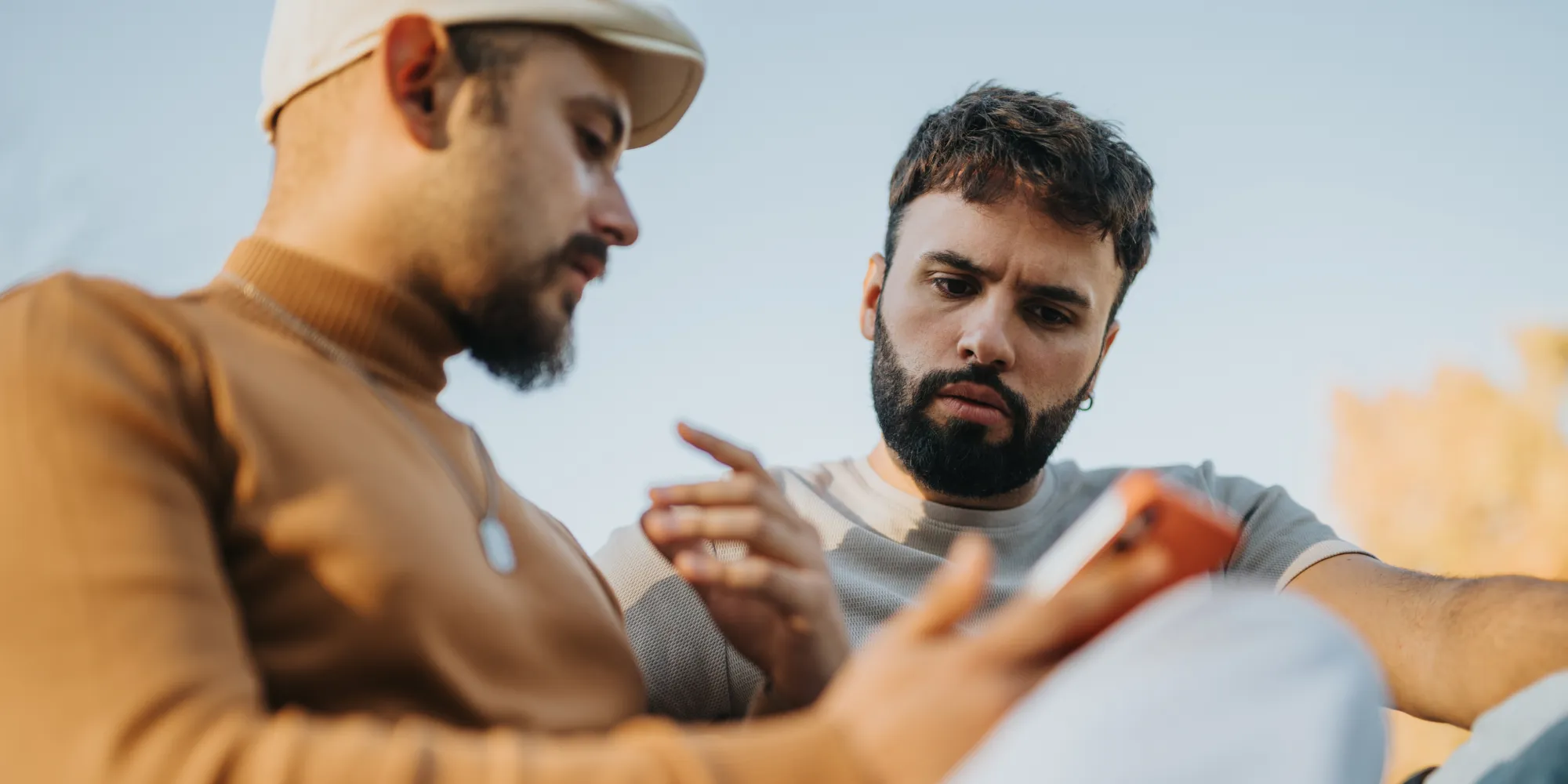 Two men looking at a smartphone screen together outdoors, discussing digital content.